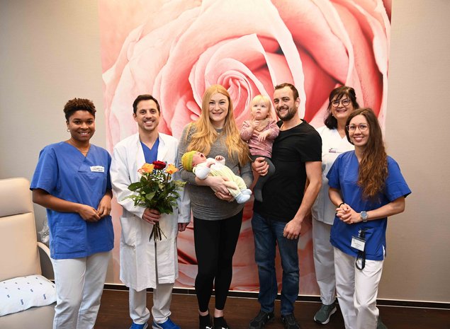 Im Bild von links nach rechts:  Hebamme Marie Diatta, Oberarzt Matey Ikonomov, Mutter Marion Hane mit Aurel, Vater Max Hane mit Rosmarie, Pflegefachkraft Daniela Kübler und Assistenzärztin Luca-Patricia Laszlo.